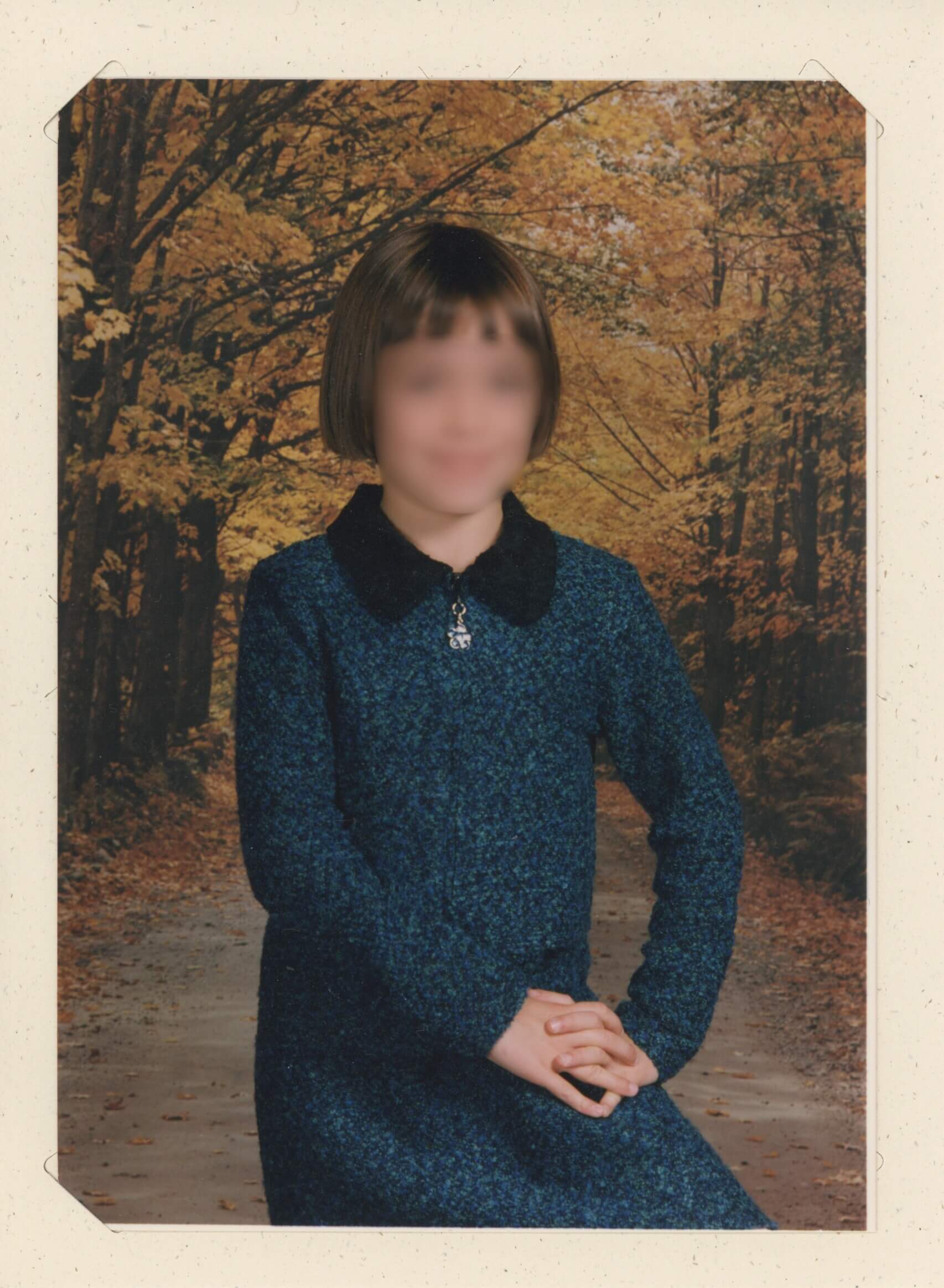 My 2nd grade picture day photo, I have on a blue fuzzy dress with a black collar. The background features fall foliage.